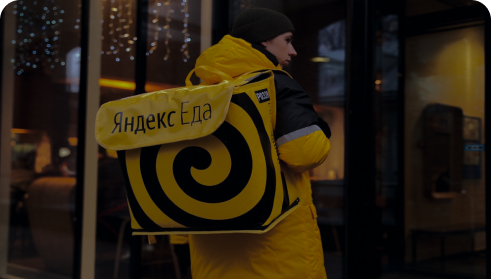 Курьер Яндекс Еды на фоне кафе